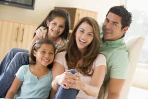 Orthodontic patient family concept - Family sitting in living room smiling to camera, sitting down.
