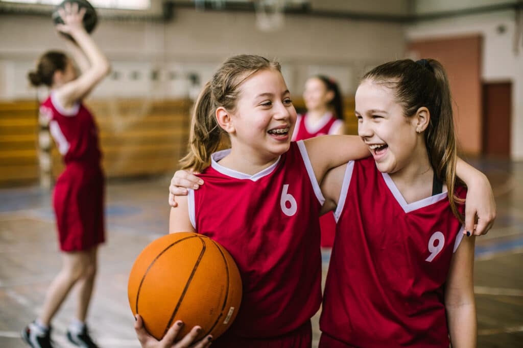 Happy teenage girls, one with braces, playing basketball.