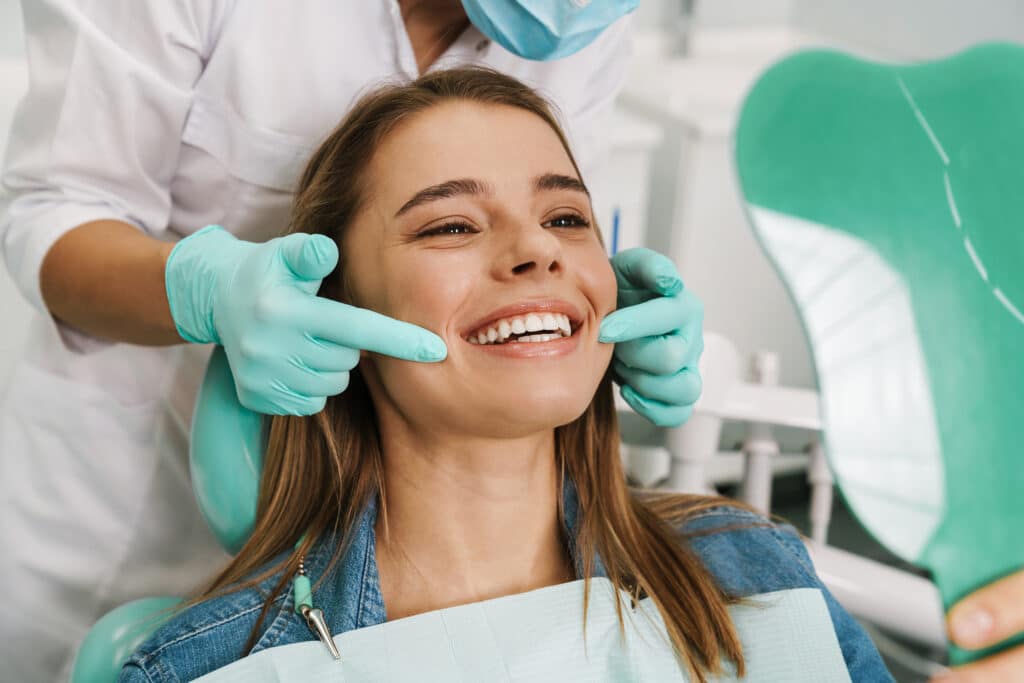 Smiling happy orthodontic patient pictured in the clinic chair, being examined by orthodontist.