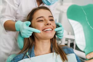 Smiling happy orthodontic patient pictured in the clinic chair, being examined by orthodontist.