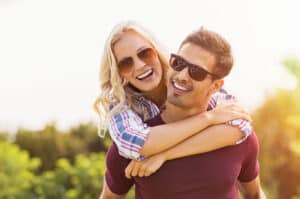Invisalign lifestyle shot - Smiling boyfriend giving smiling girlfriend piggyback ride whilst outdoors.