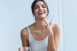 Woman about to clean Invisalign, toothbrush and glass of water in her hands, pointing to her teeth.