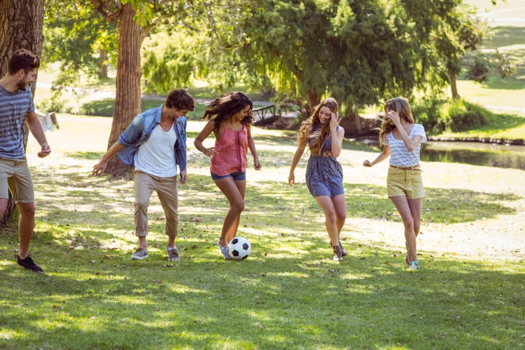 Invisalign lifestyle concept - carefree, relaxed young men and woman playing soccer in a park.