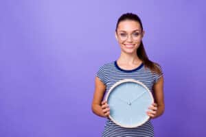 Woman wondering how long does Invisalign take, smiling and holding a clock to demonstrate the concept.