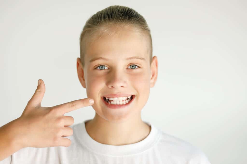 Girl wondering "what is orthodontics?" while smiling and pointing to her teeth.