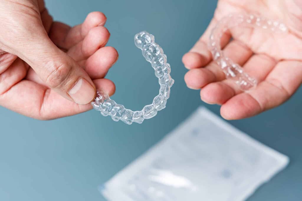 Clear aligners shown held in hands, packaging seen below.