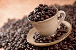 A mug overflowing with rich dark roasted whole coffee beans.