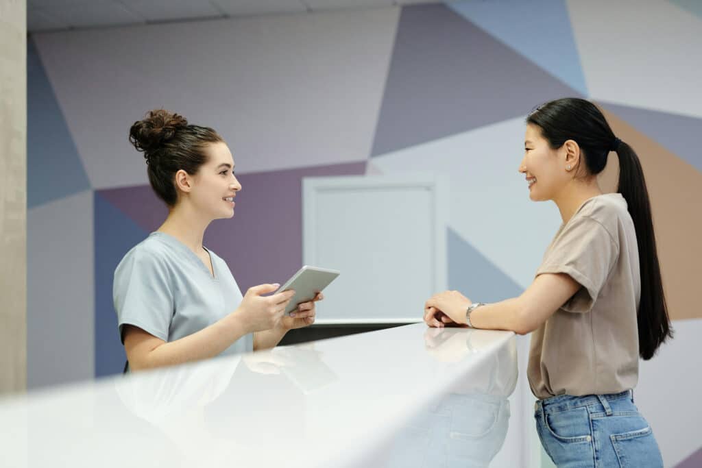 Orthodontic reception desk - patient asking receptionist a question, both smiling.