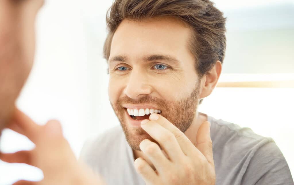 Man looking into the mirror wondering if his teeth have shifted after braces treatment.